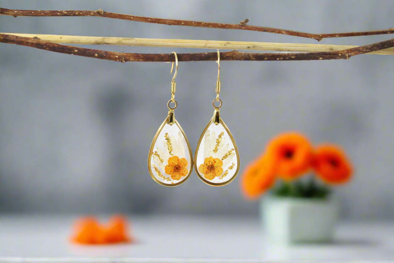 Handmade teardrop earrings featuring real pressed white daisy petals and small orange flowers encased in a gold metal frame, capturing the delicate beauty of nature in a timeless, elegant design